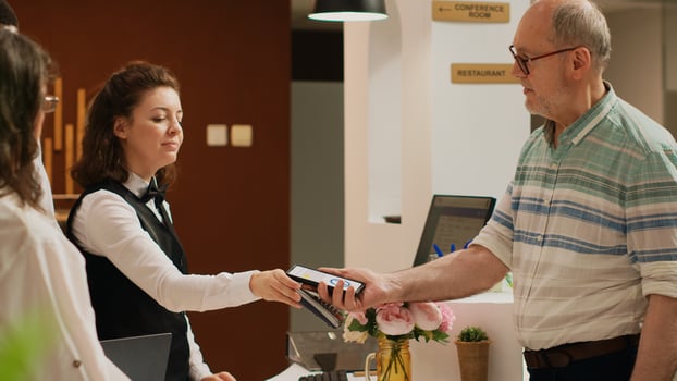Old tourist using mobile nfc technology to pay for luxury all inclusive hotel room on international vacation. Senior person putting smartphone next to pos terminal, electronic hoiday payment. photo