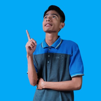 Excited Asian man wearing blue t-shirt pointing to copy space on side, isolated white background. photo