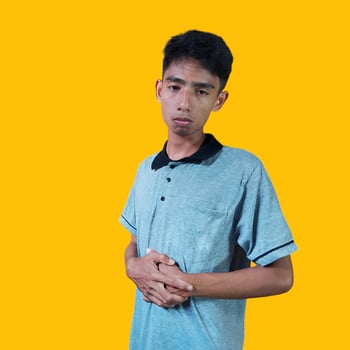 Young Asian man holding stomach in pain wearing gray t-shirt. isolated yellow background. photo