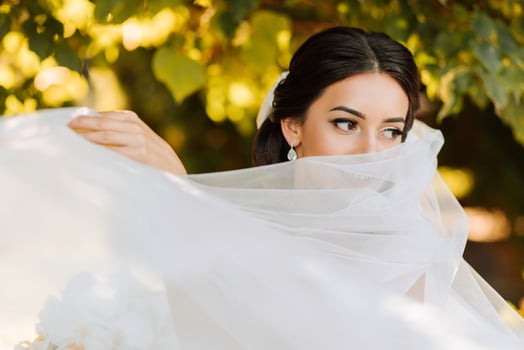 Warm sunny portrait of a happy bride with a bouquet of orchids in her hands, outdoors and at sunset. Warm summer time. A long veil, a luxurious white dress with a train. photo
