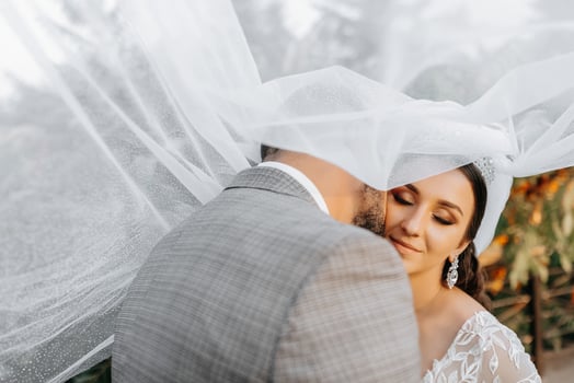 Young wedding couple enjoying romantic moments outdoors on a summer meadow. A bride with a crown on her head and a long veil. Groom in a classic gray suit photo