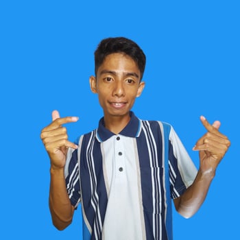 Young Asian man feeling happy and romantic forming heart gesture, wearing colorful t-shirt on blue background. photo
