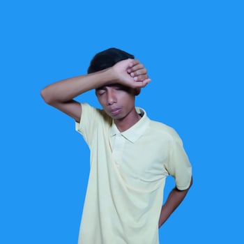 young Asian man crying holding both fists over eyes, wearing blue shirt. isolated blue background. photo
