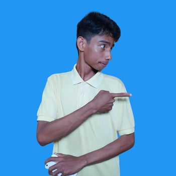 excited asian man wearing yellow t-shirt pointing to the copy space on the side blue background. photo