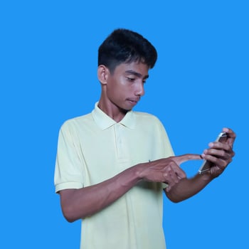 Young asian man surprised looking at smart phone isolated blue background. wearing a yellow t-shirt photo