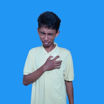 Young Asian man pressing chest painful expression, heart attack, cramps. isolated blue background. photo