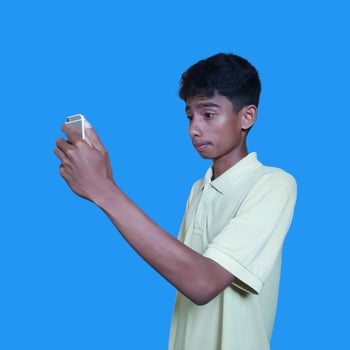 Young asian man surprised looking at smart phone isolated blue background. wearing a yellow t-shirt photo