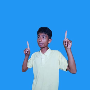 excited asian man wearing yellow t-shirt pointing to the copy space on the side blue background. photo