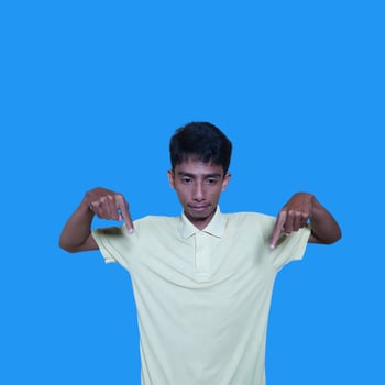excited asian man wearing yellow t-shirt pointing to the copy space on the side blue background. photo