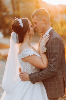 A fabulous romantic newlywed couple is hugging at sunset in an autumn park with leaves from trees on the grass photo