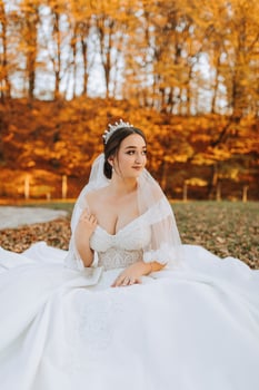 A beautiful bride is sitting on the grass near the autumn leaves of the trees. Wedding portrait of a young bride in an autumn theme. Wedding photography. photo