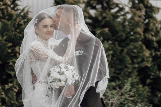 The bride in an elegant dress with a bouquet and the groom in a classic suit are walking in the garden, holding hands. photo