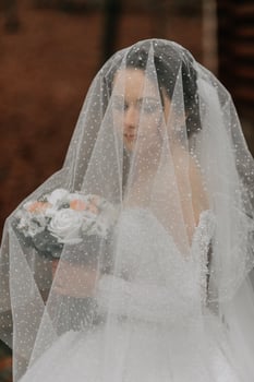 The bride in a white voluminous dress with a long train holds a bouquet and poses while walking in the forest. Winter wedding. photo