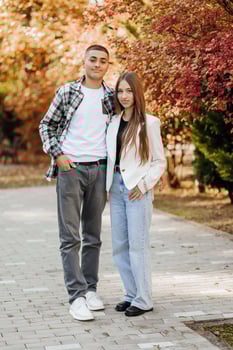 Vertical photo of two teenage friends dressed in casual clothes standing next to each other against a background of nature. Best school friends are ready to overcome anything to achieve the goal.