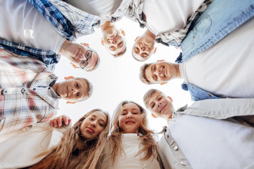 Large group of smiling young people standing, hugging, looking at camera. Group of cheerful teenage people in a circle looking down. Low viewing angle. Copy space. photo