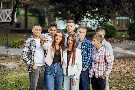 Friends taking a big group selfie smiling at the camera - laughing young people standing outdoors and having fun - portrait of cheerful schoolchildren outside school - human resources concept photo