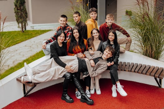 Group of smiling and happy teenage friends wearing casual clothes spending time together, posing and talking with each other near college building on autumn day. photo