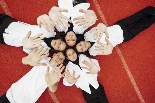 Happy friends lying together in a circle looking at the camera, holding hands and smiling while lying on a red wall... Friendship, lifestyle, togetherness, business and teamwork concepts. photo
