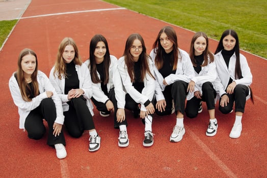 A group of many happy teenage girls dressed in the same outfit having fun and posing in a stadium near a college. Concept of friendship, moments of happiness. School friendship photo
