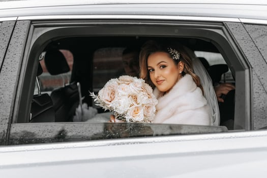 Portrait of an incredibly beautiful bride in the window of an expensive car. The bride with a bouquet of flowers looks into the camera lens. photo