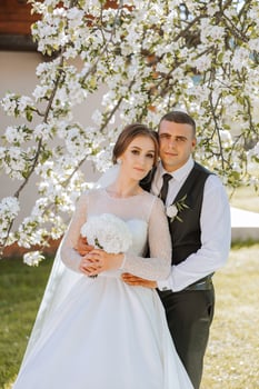 Wedding. Love and couple in garden for wedding. Celebration of ceremony and commitment. Save the date. Trust. The bride and groom embrace. The groom embraces the bride under a spring flowering tree. photo