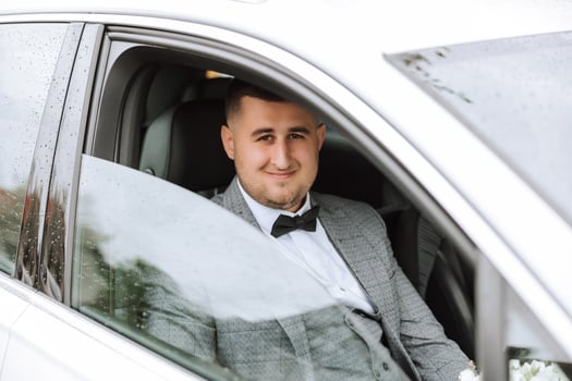 a handsome groom sits with a wedding bouquet inside a white car and looks out the window. A happy moment on the wedding day. photo