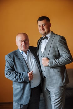 A father hugs his mature son and helps him prepare for the wedding ceremony. Warm and sincere relations between a father and an adult son. An emotional moment at a wedding photo