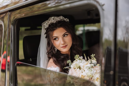 A beautiful bride, sitting in a car, looks out of the open window of the car. A beautiful bride with a bouquet of flowers in her hands is sitting in a stylish expensive car. photo