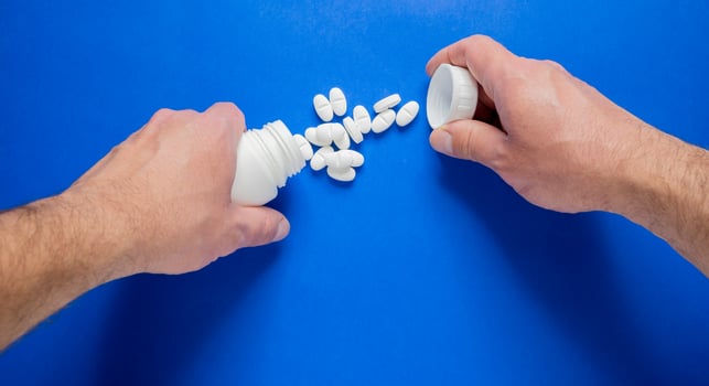 Hands opening a bottle of white pills on a table. photo