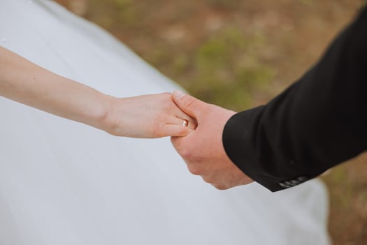 The groom holds the bride's hand. Cropped photo. Groom in a black suit. Details photo