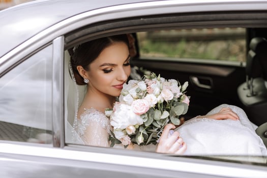 A beautiful bride, sitting in a car, looks out of the open window of the car. A beautiful bride with a bouquet of flowers in her hands is sitting in a stylish expensive car. photo