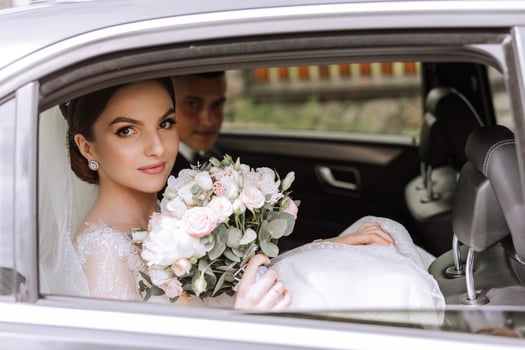 A beautiful bride, sitting in a car, looks out of the open window of the car. A beautiful bride with a bouquet of flowers in her hands is sitting in a stylish expensive car. photo