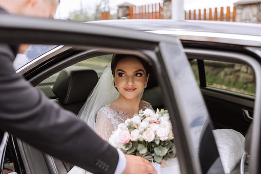 A beautiful bride, sitting in a car, looks out of the open window of the car. A beautiful bride with a bouquet of flowers in her hands is sitting in a stylish expensive car. photo