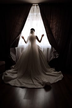 A luxurious bride with a beautiful hairstyle and a gorgeous dress is getting ready for the wedding ceremony in the morning. Morning photo of the bride at home or in a hotel room. Professional makeup.