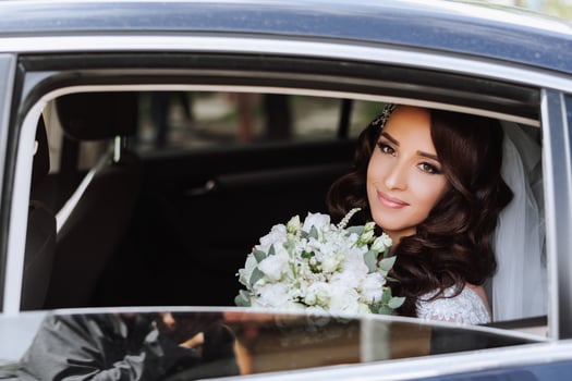 A beautiful bride, sitting in a car, looks out of the open window of the car. A beautiful bride with a bouquet of flowers in her hands is sitting in a stylish expensive car. photo