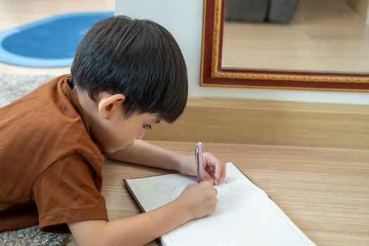 A little Asian boy was lying on the floor drawing on paper. photo