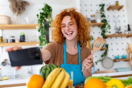 Young woman is in the kitchen, she has wireless headphones on, she is dancing and singing photo