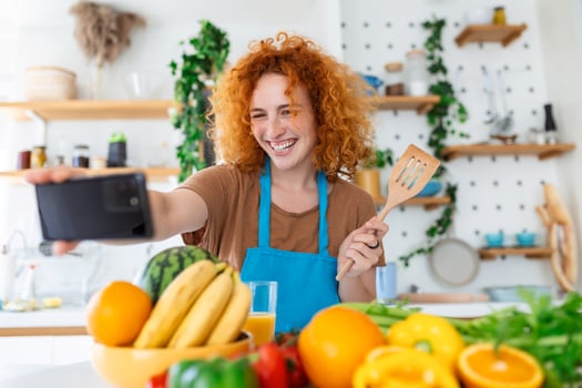 Young woman is in the kitchen, she has wireless headphones on, she is dancing and singing photo