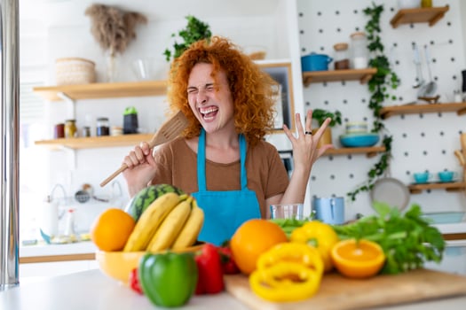Funny beautiful woman singing into spatula, cooking in modern kitchen, holding spatula as microphone, dancing, listening to music, playful girl having fun with kitchenware, preparing food. photo
