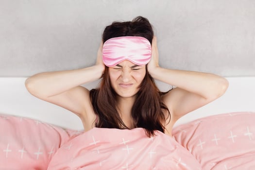 A beautiful girl sits in bed in pajamas and a sleep mask. Woman cannot sleep, the neighbors are noisy or she have headache Pink bed linen photo