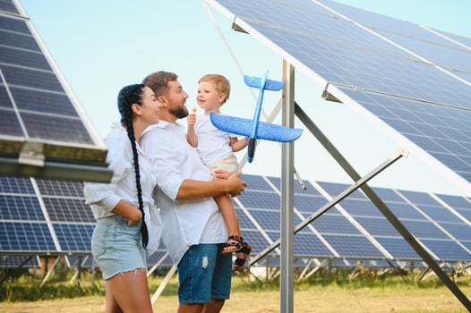 A wide shot of a happy family standing together and smiling at camera with a large solar panel in background photo