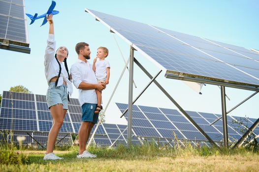 A wide shot of a happy family standing together and smiling at camera with a large solar panel in background photo