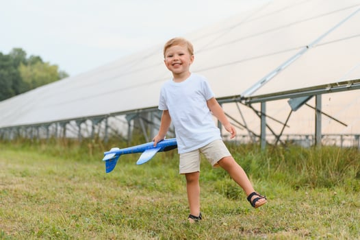 Little happy boy playing with toy airplane near solar panels. photo