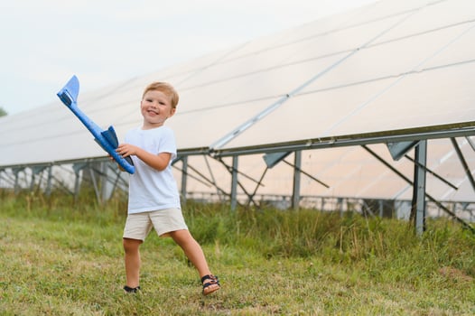 Little happy boy playing with toy airplane near solar panels. photo