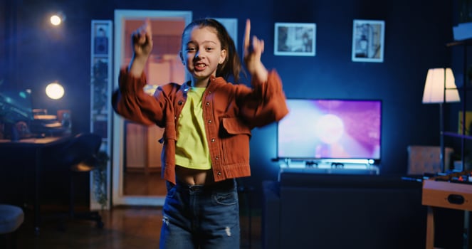 Happy young kid doing viral dance choreography, creating content to generate views and engagement. Cute girl having fun dancing around living room, entertaining audiences photo