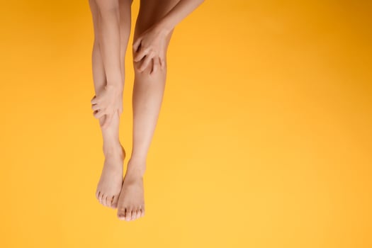 Explore legs healthcare with a close up of woman's legs, hands holding her pained legs on a vibrant yellow background. Concept of leg pain relief. photo