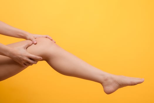 Knee pain, woman hands holding pain knee isolated on yellow background. concept of legs and knee healthcare photo