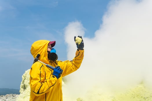 woman volcanologist on the background of a smoking fumarole examines a sample of a sulfur mineral photo