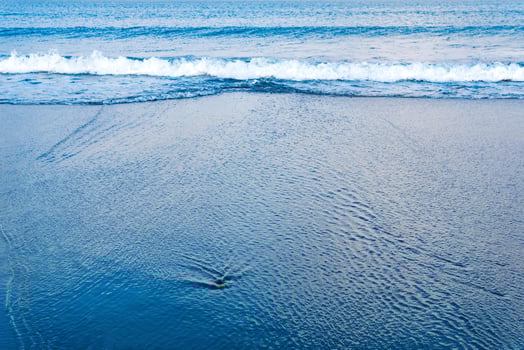 ocean beach with a wave coming back, in which the sky is reflected photo