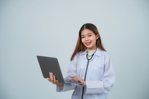 Portrait asian doctor woman using laptop, intern with stethoscope and medical robe, professional, cross arms, looking confident at camera, grey or white background. photo